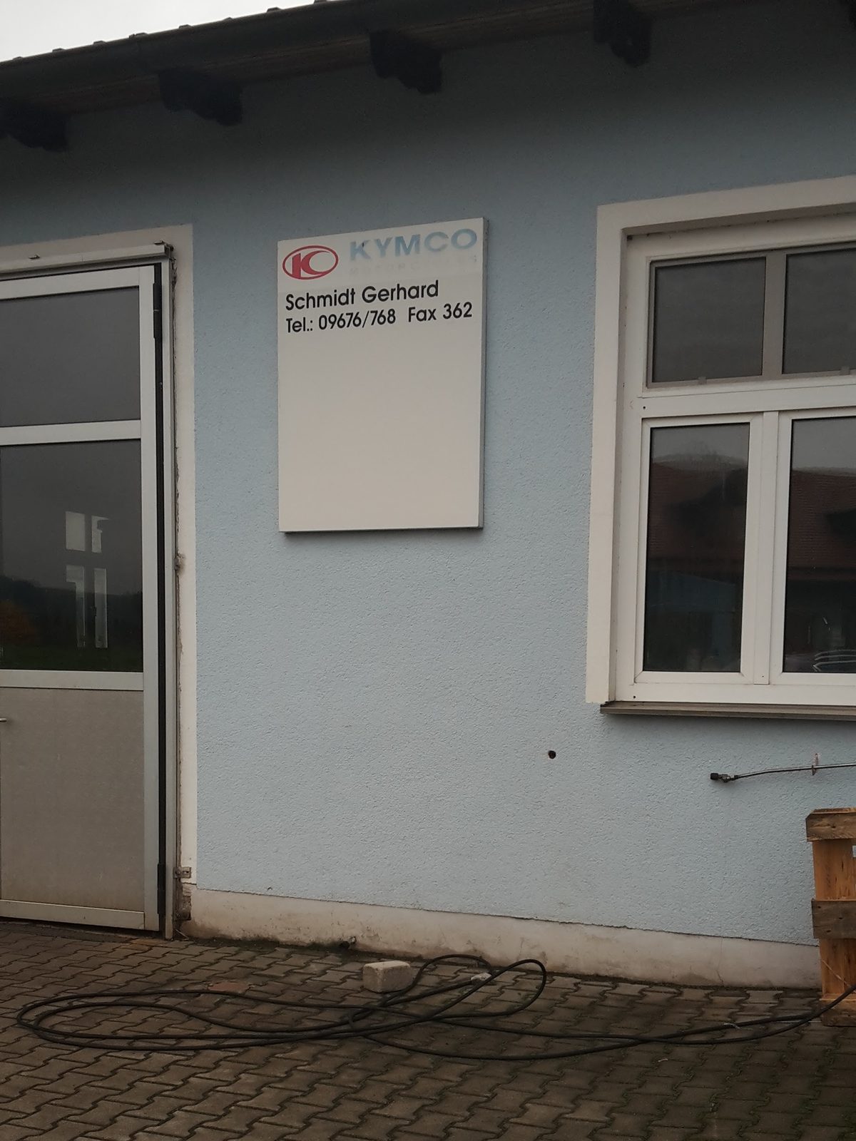 Werkstatttür und weißes Schild mit Kymco-Logo, Schmidt Gerhard, Tel.: 09676/768, Fax 362