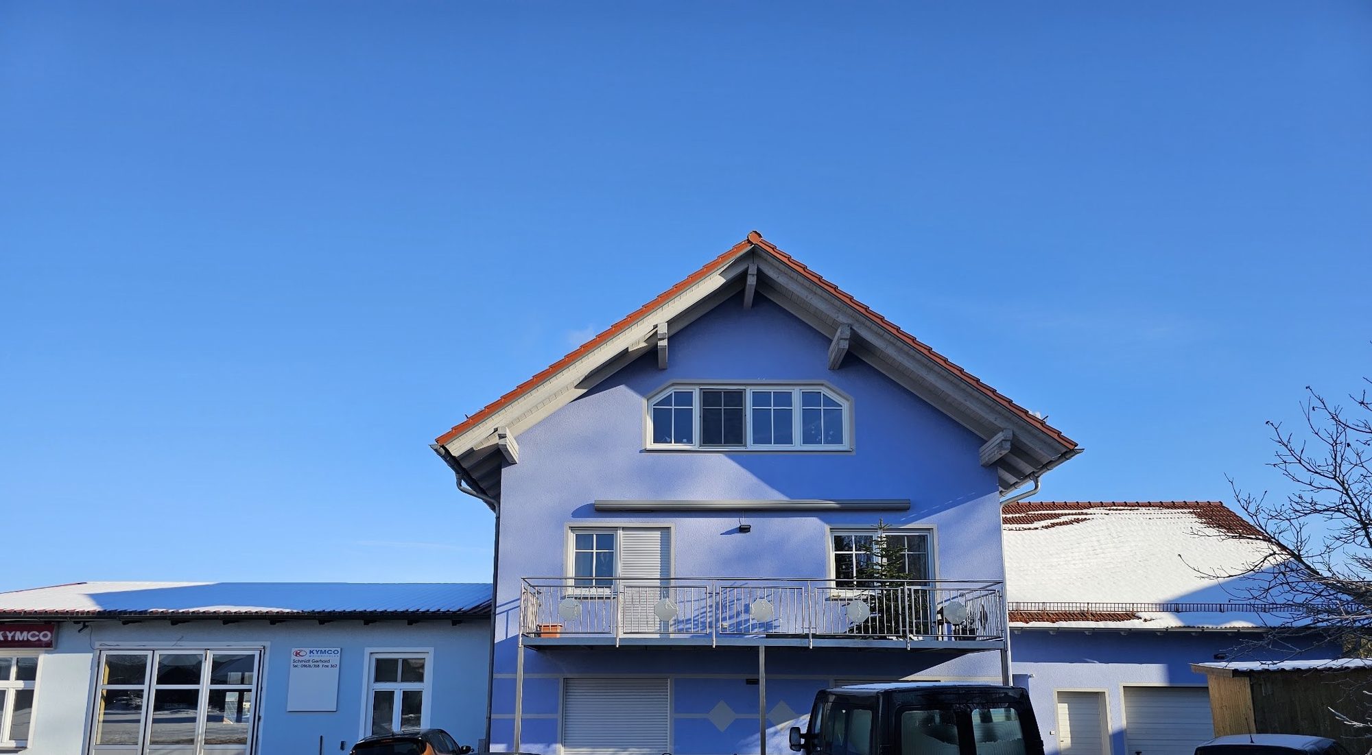 Blaues Wohnhaus mit angebautem Werkstattflügel und Kymco-Schild in Winklarn-Schneeberg, blauer Winterhimmel